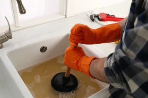 Homeowner in O’Fallon, IL, using a plunger to clear clog out of their drain with backed-up water in the sink.