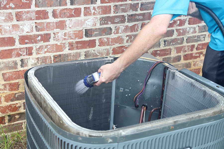 Technician using a hose to clean out the dirt on the inside of an air HVAC unit in O’Fallon, IL.